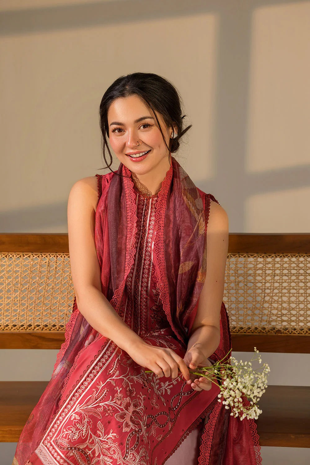 Woman in a red patterned dress sitting on a wooden bench with a neutral background