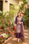 A woman stands in a garden courtyard wearing a purple traditional outfit with ornate gold and silver embroidery and a matching embroidered dupatta.