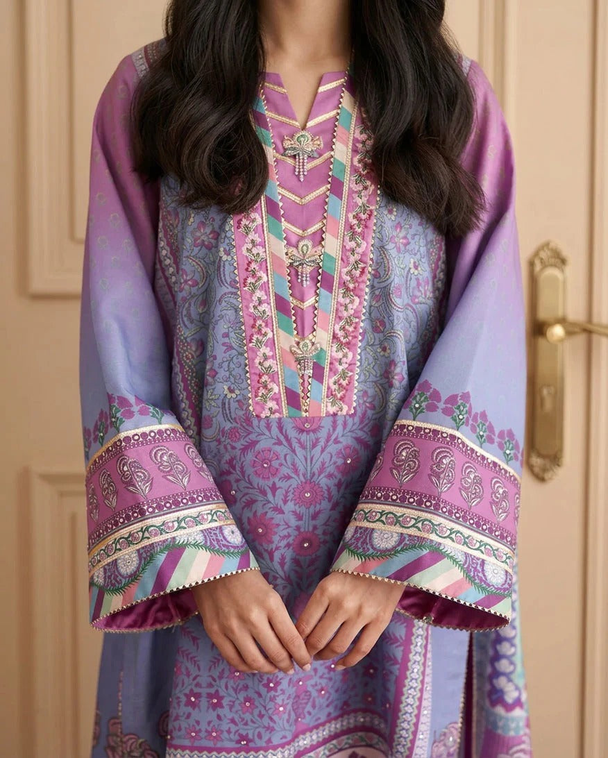 A close-up of a person wearing a traditional embroidered tunic in lavender and pink with intricate floral and geometric patterns, standing in front of a beige door.