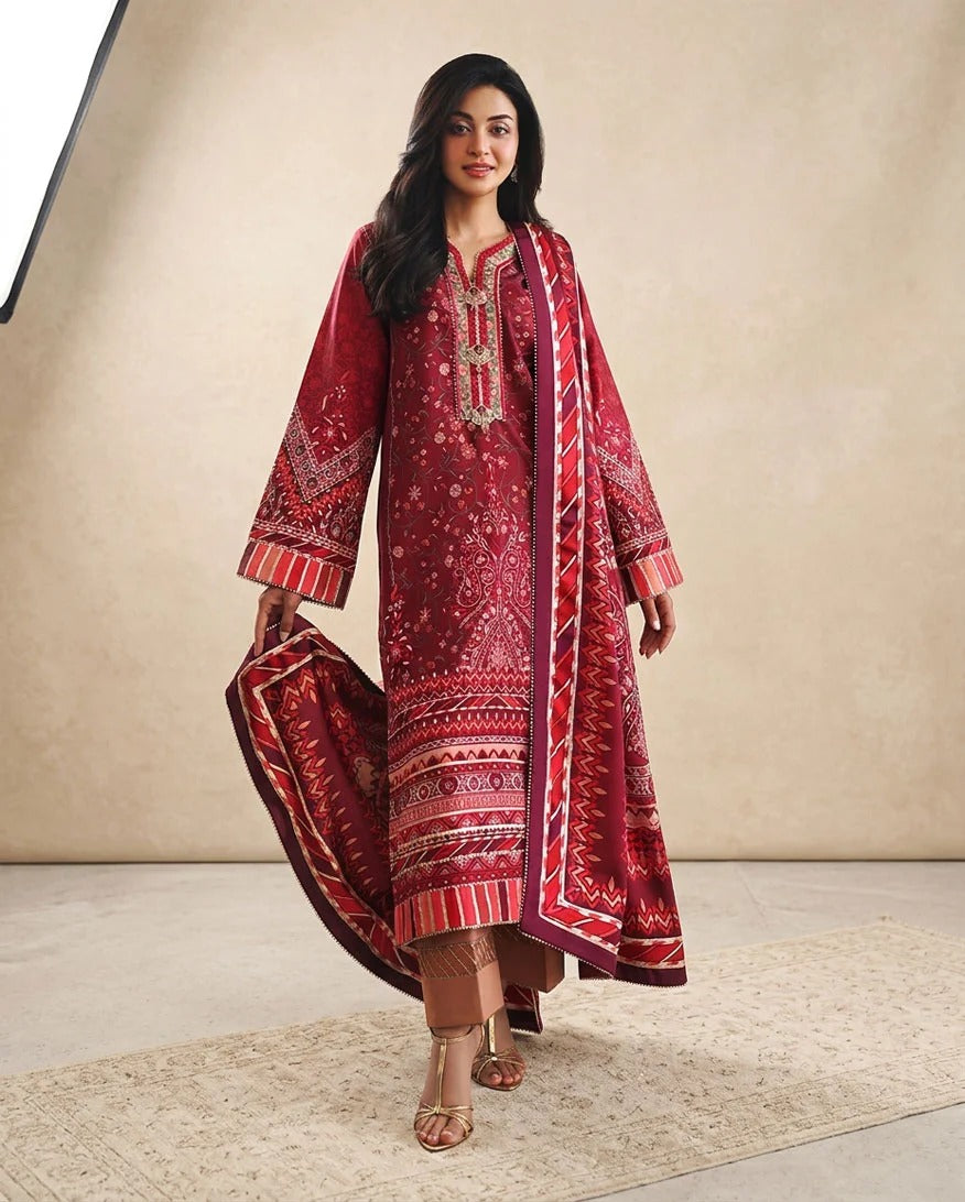 A woman models a traditional three-piece salwar kameez suit in deep red with intricate white and gold embroidery, featuring a matching embroidered dupatta, set against a neutral beige studio backdrop.