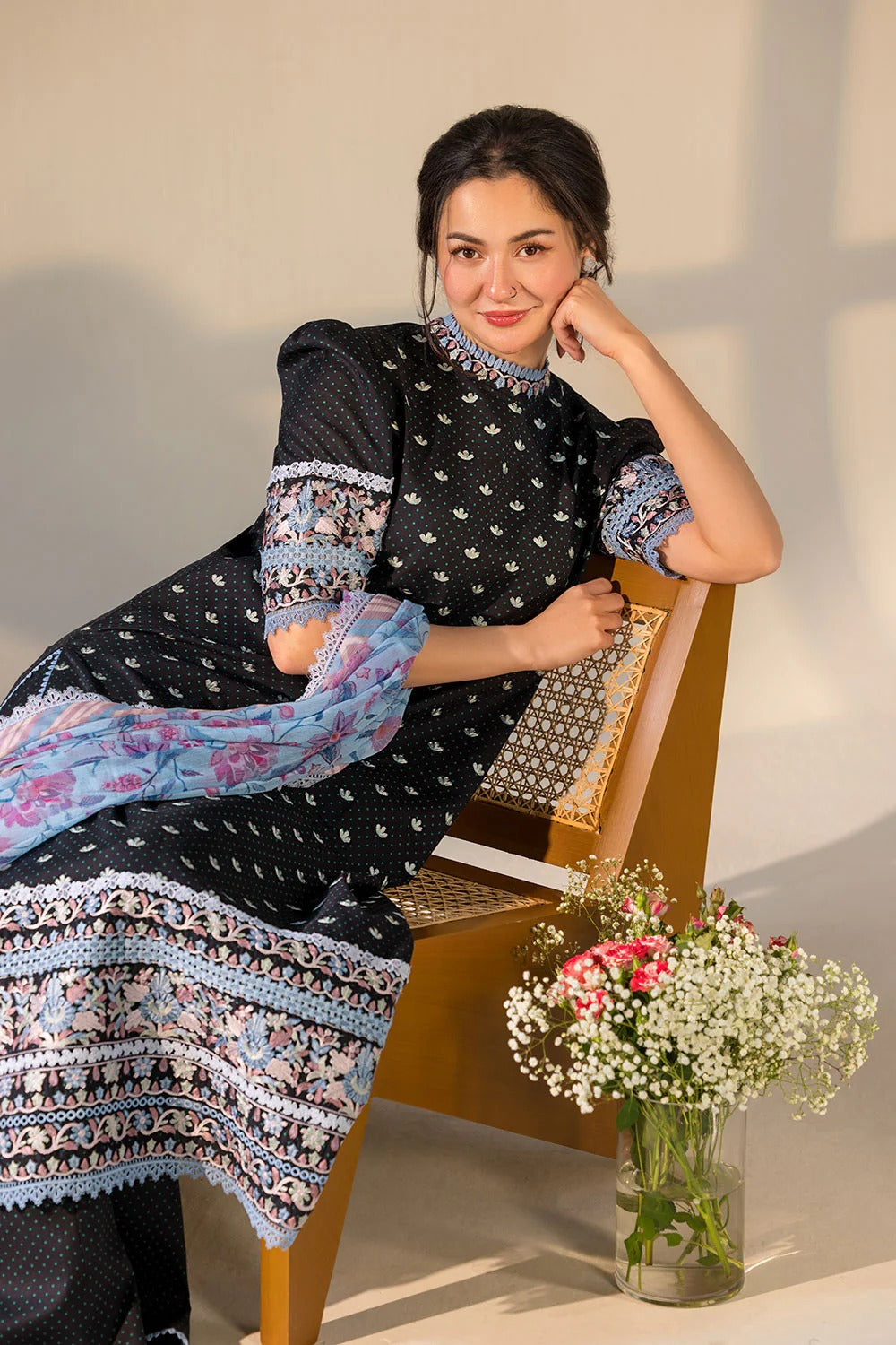 Woman in a patterned dress sitting on a chair with flowers beside her