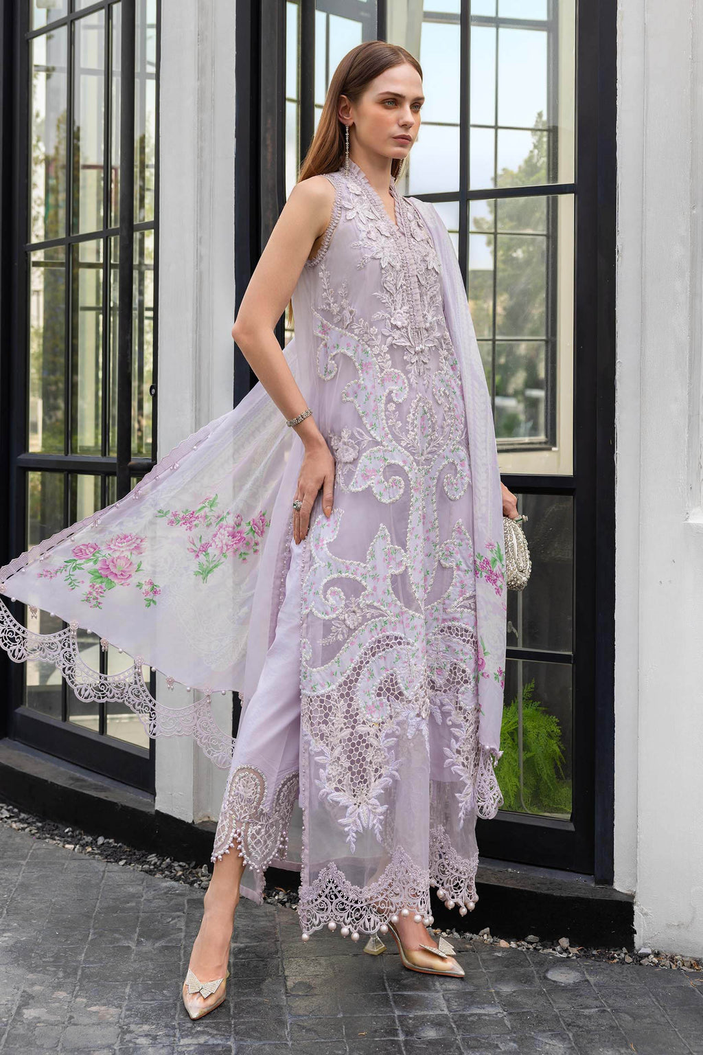 Woman wearing a light purple embroidered dress with floral details in an outdoor setting.
