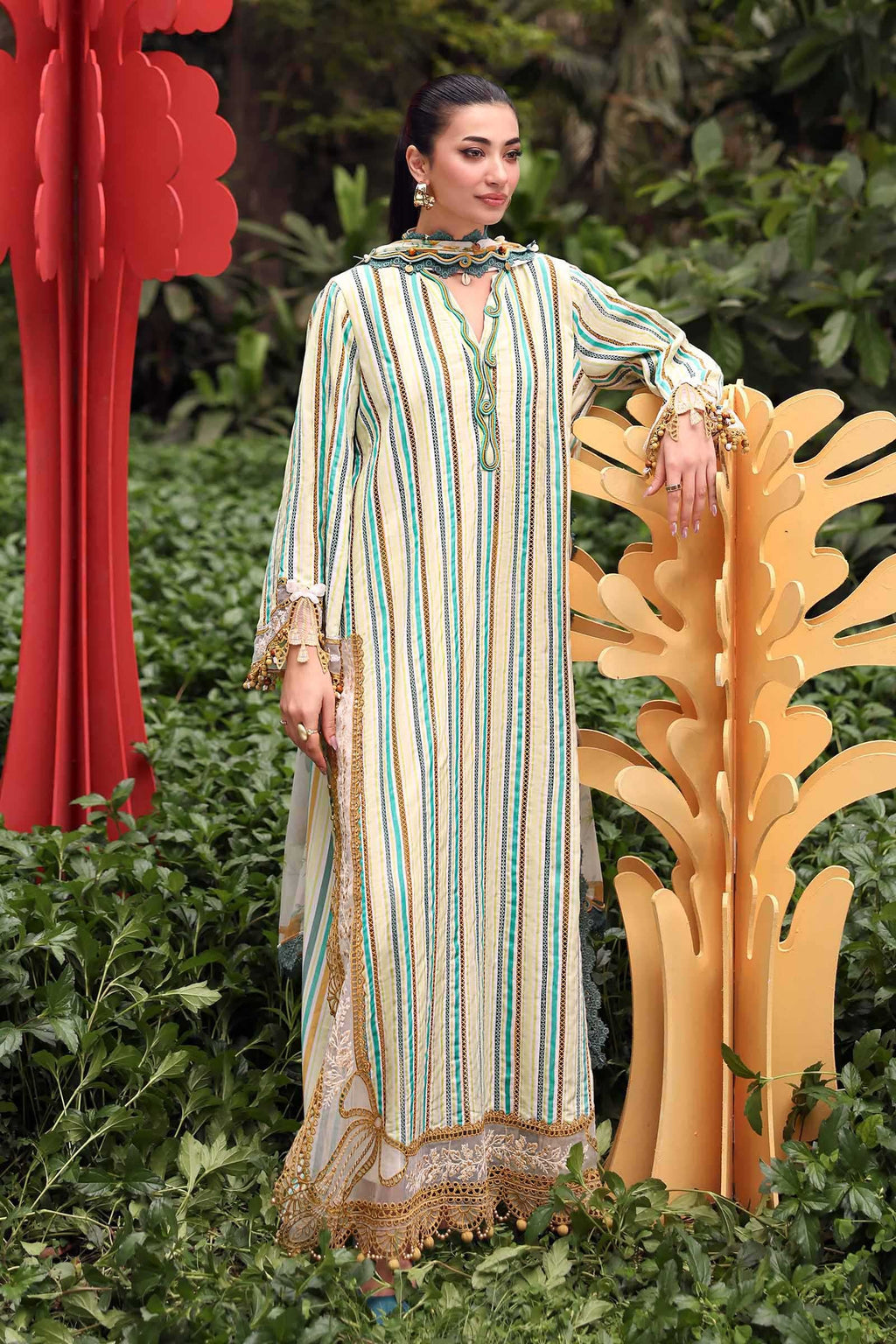 Woman in a long, striped dress standing in a garden with decorative elements.