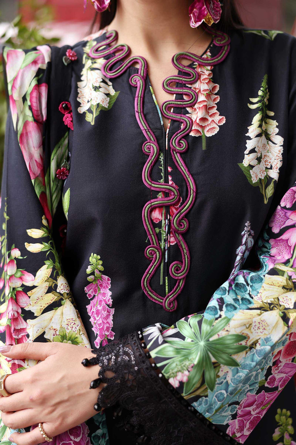 Close-up of a person wearing a black blouse with floral embroidery and colorful floral patterns on sleeves and hem.