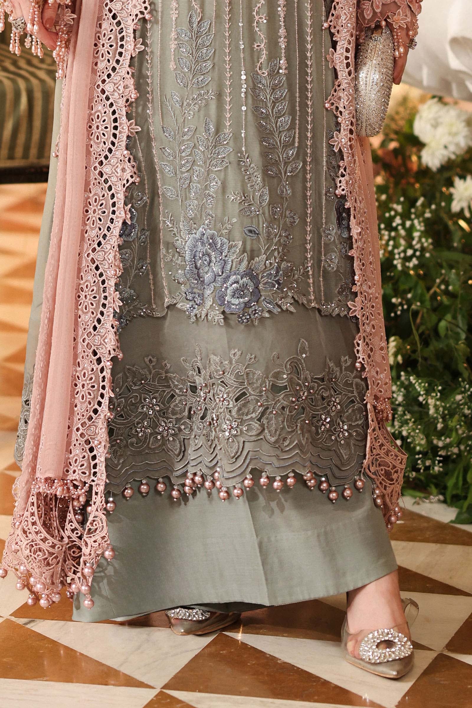 A close-up of a traditional South Asian outfit featuring a sage green embroidered kurta with pink lace borders and a matching pink dupatta, shown on a model standing on a tiled floor.
