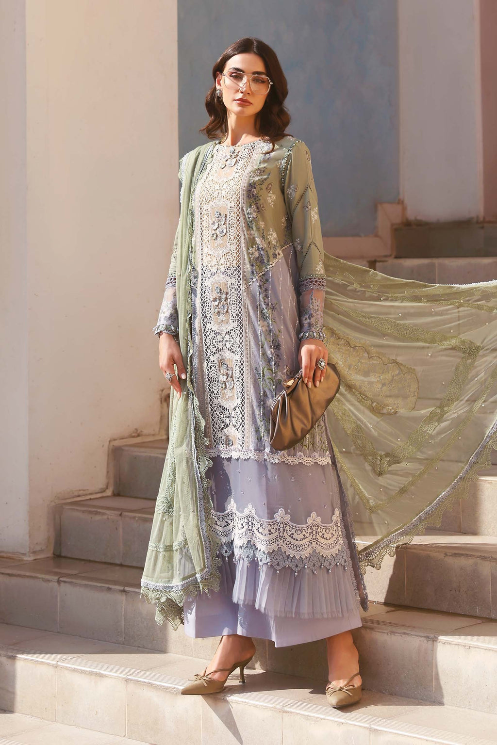 Woman in a light green and purple traditional outfit with a sheer dupatta, standing on steps.