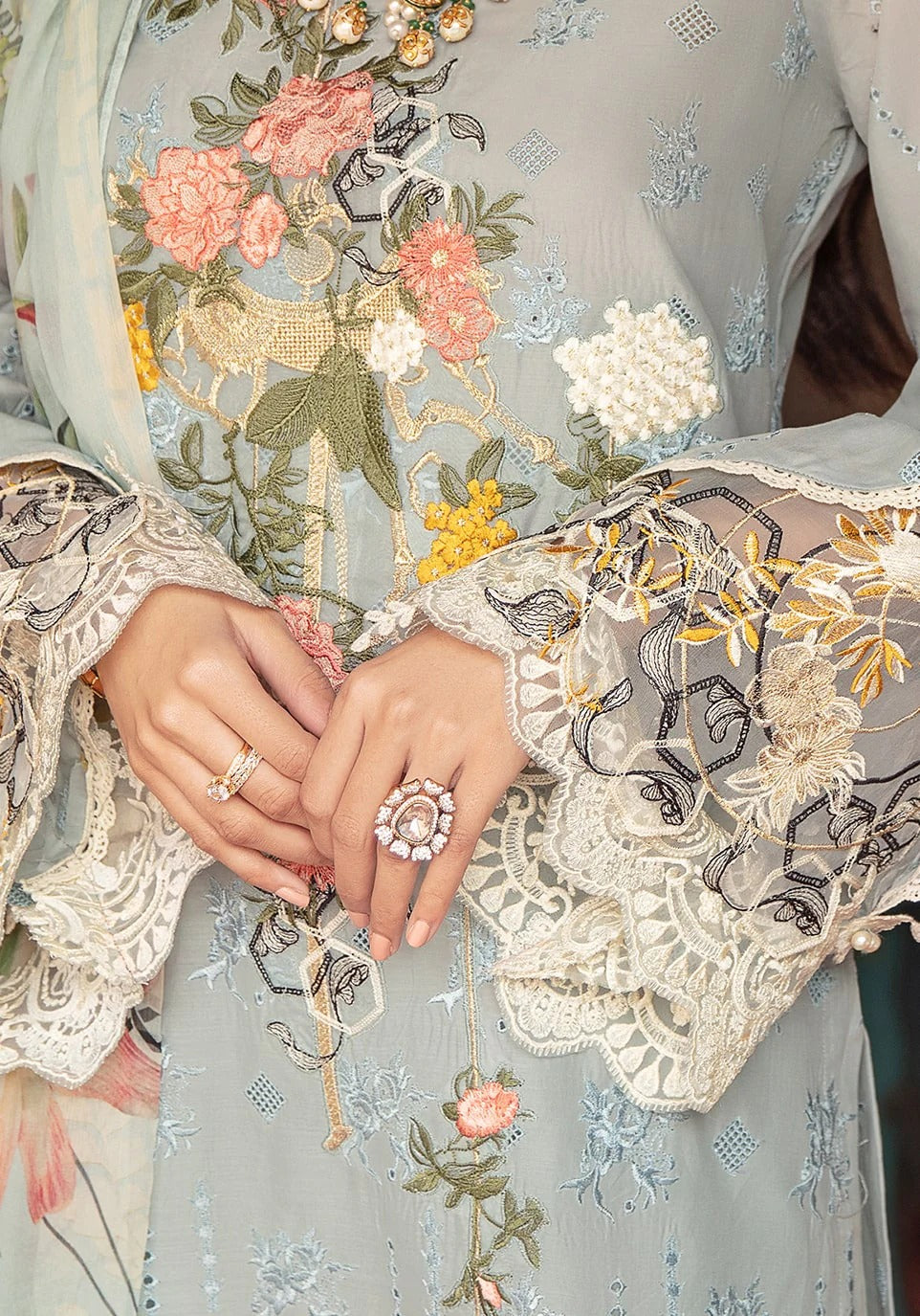 Close-up of a light blue-green embroidered traditional outfit with floral embroidery, lace sleeves, and a matching dupatta, shown on a model with hands visible.