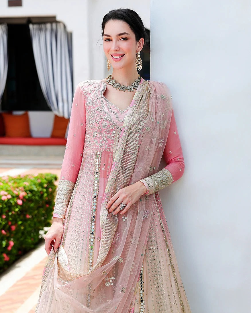 A woman models a traditional pink and beige embroidered Indian outfit with a matching sheer dupatta, standing against a white wall.