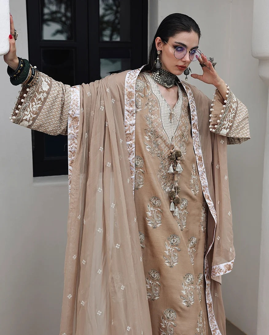 A model wearing a traditional beige embroidered kurta set with a matching sheer dupatta and a long beige coat with white floral embroidery, styled with statement jewelry.