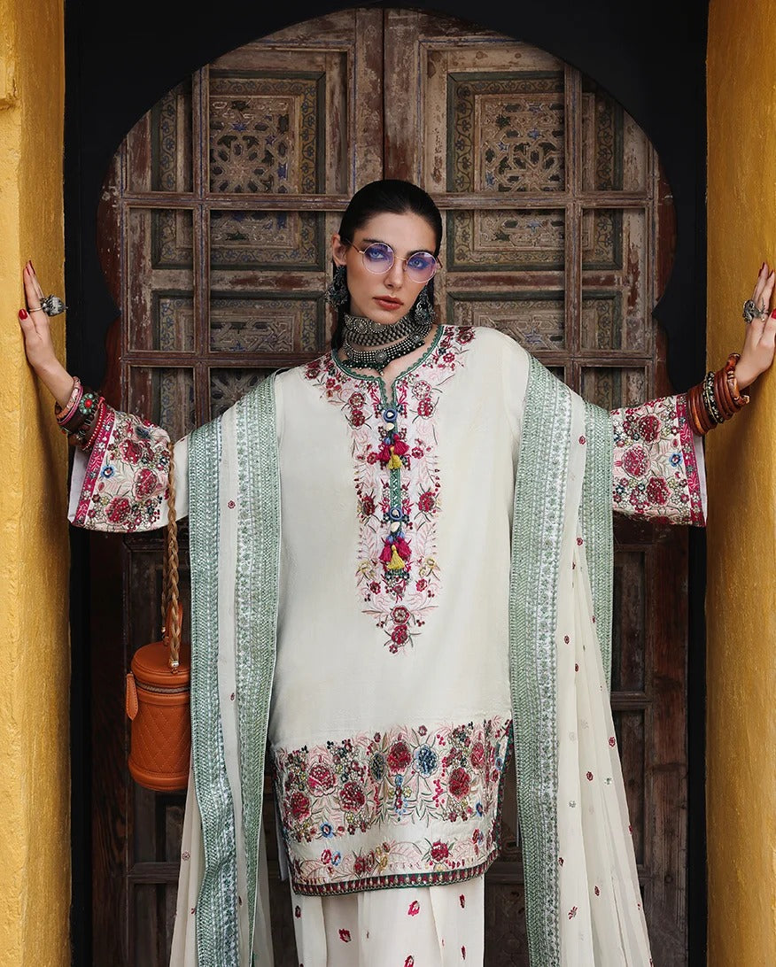 A model wearing a traditional embroidered white salwar kameez suit with a mint green dupatta, posing in front of an ornate wooden door.