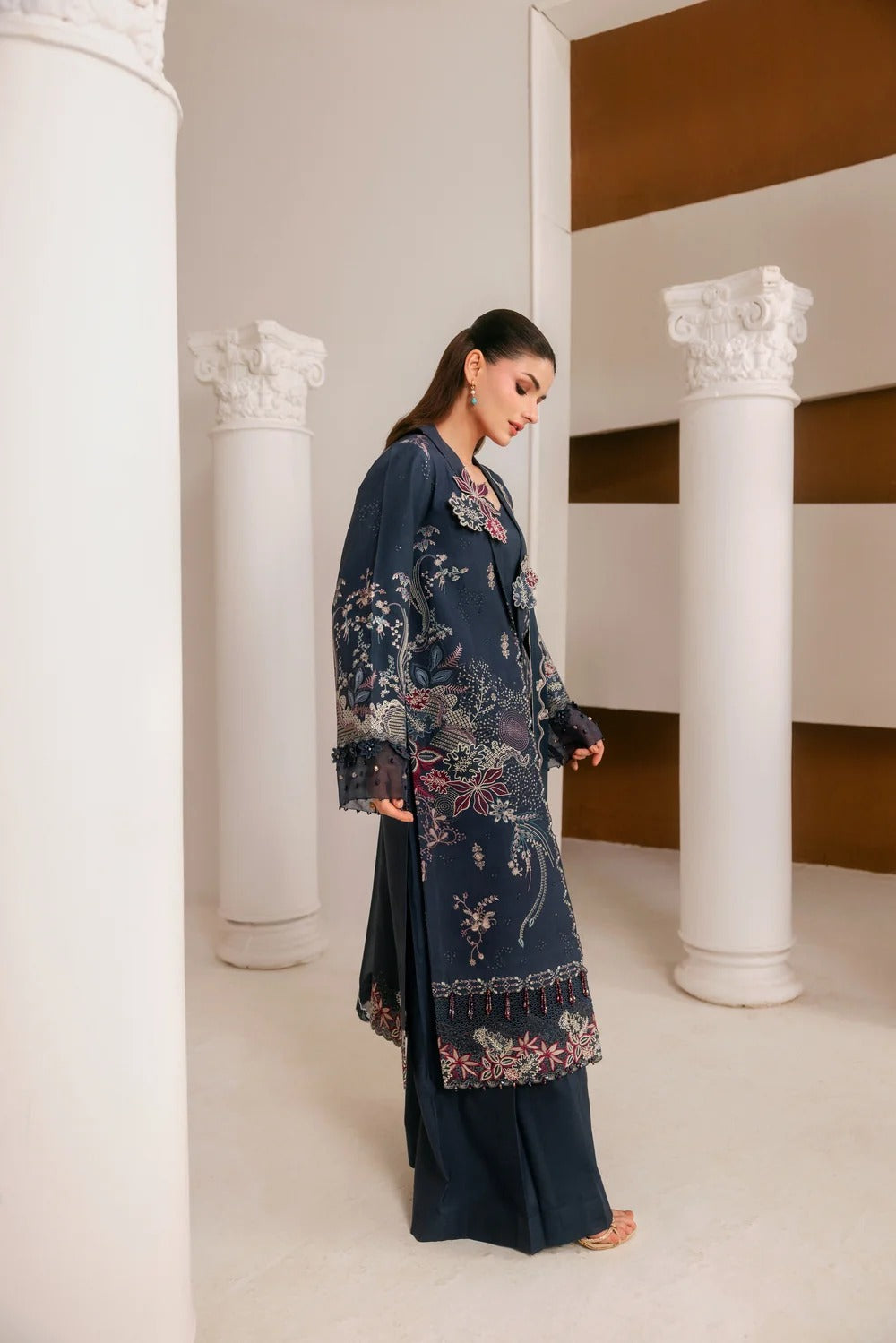 A woman modeling a dark navy blue embroidered kurta set with matching wide-leg trousers, standing in a classical interior with white columns.