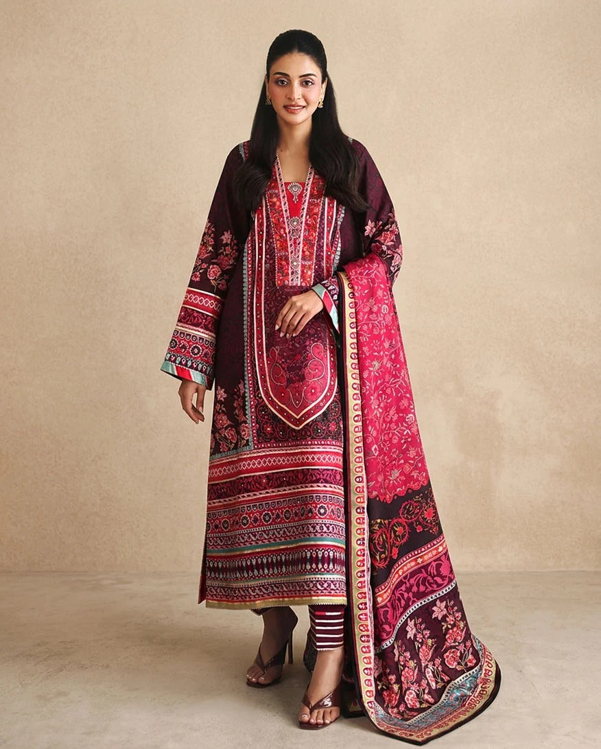 A woman modeling a traditional three-piece ethnic suit set featuring a deep maroon kurta with intricate red and pink floral patterns, a matching maroon jacket, and a coordinating dupatta draped over her shoulder, set against a neutral beige background.