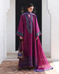 A woman models a traditional magenta purple ethnic outfit with intricate teal and gold embroidery, a matching long dupatta, and a small brown handbag, standing in front of a dark doorway.