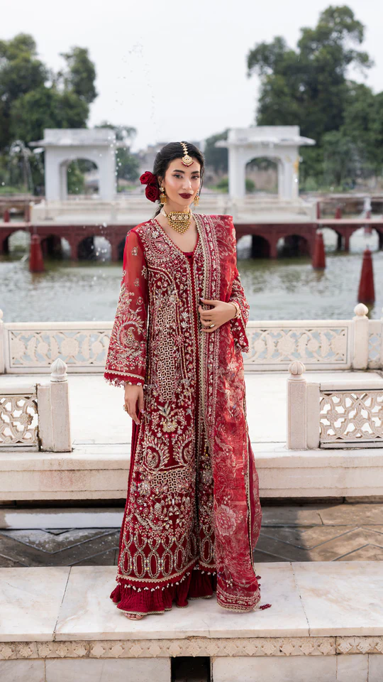 Woman in a red embroidered traditional outfit standing in front of a water body with architectural structures.