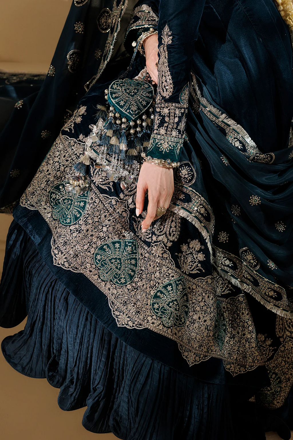 A close-up of a dark navy blue traditional outfit with intricate silver and teal embroidery, featuring a ruffled skirt, embroidered sleeves, and a matching dupatta.