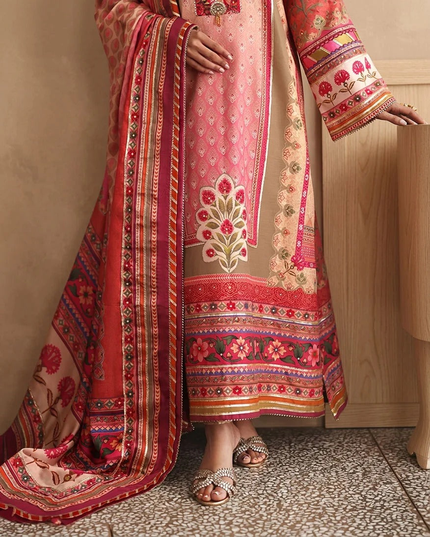 A model wears a traditional South Asian salwar kameez suit in pink and beige with intricate floral embroidery and a matching patterned dupatta, standing in an indoor setting.