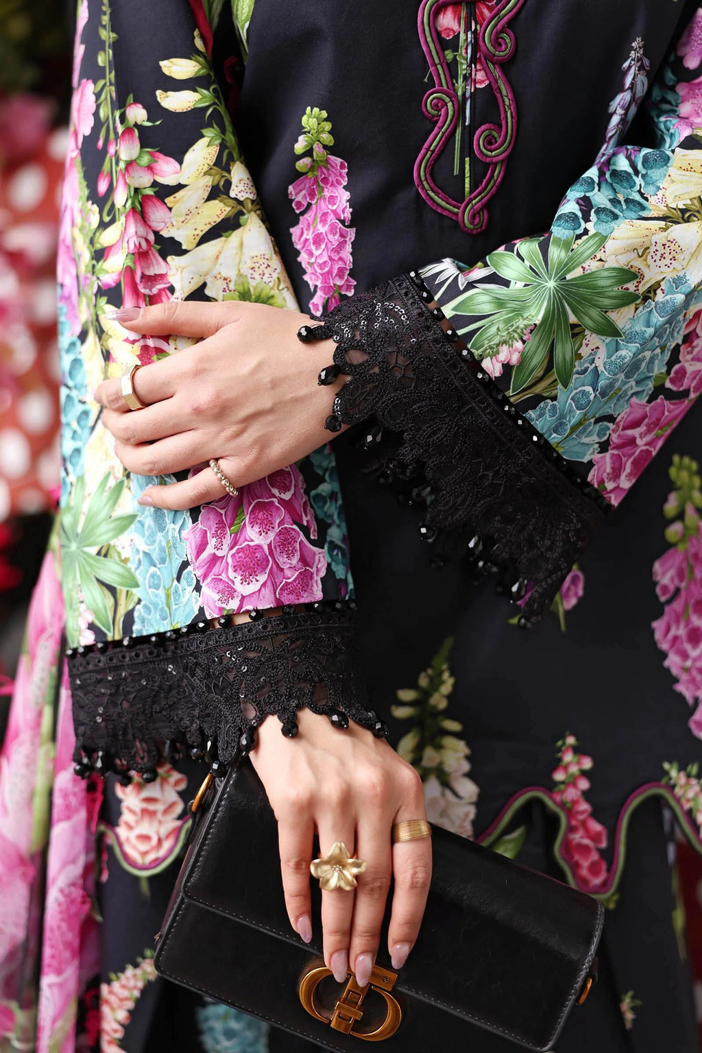 Close-up of a person wearing a colorful floral dress with black lace sleeves, holding a black clutch.