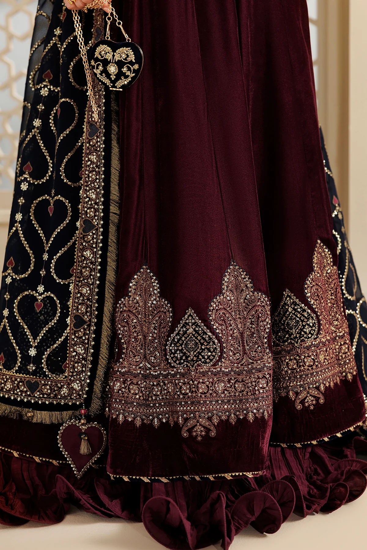 Close-up of a traditional Indian ethnic wear garment, featuring a deep maroon velvet skirt with intricate gold and silver embroidery, paired with a black embroidered dupatta.