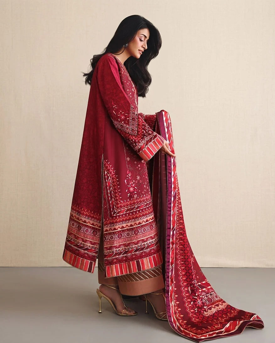 A woman models a traditional three-piece salwar kameez suit in deep red with intricate white and gold embroidery, paired with a matching patterned dupatta, set against a neutral beige textured backdrop.