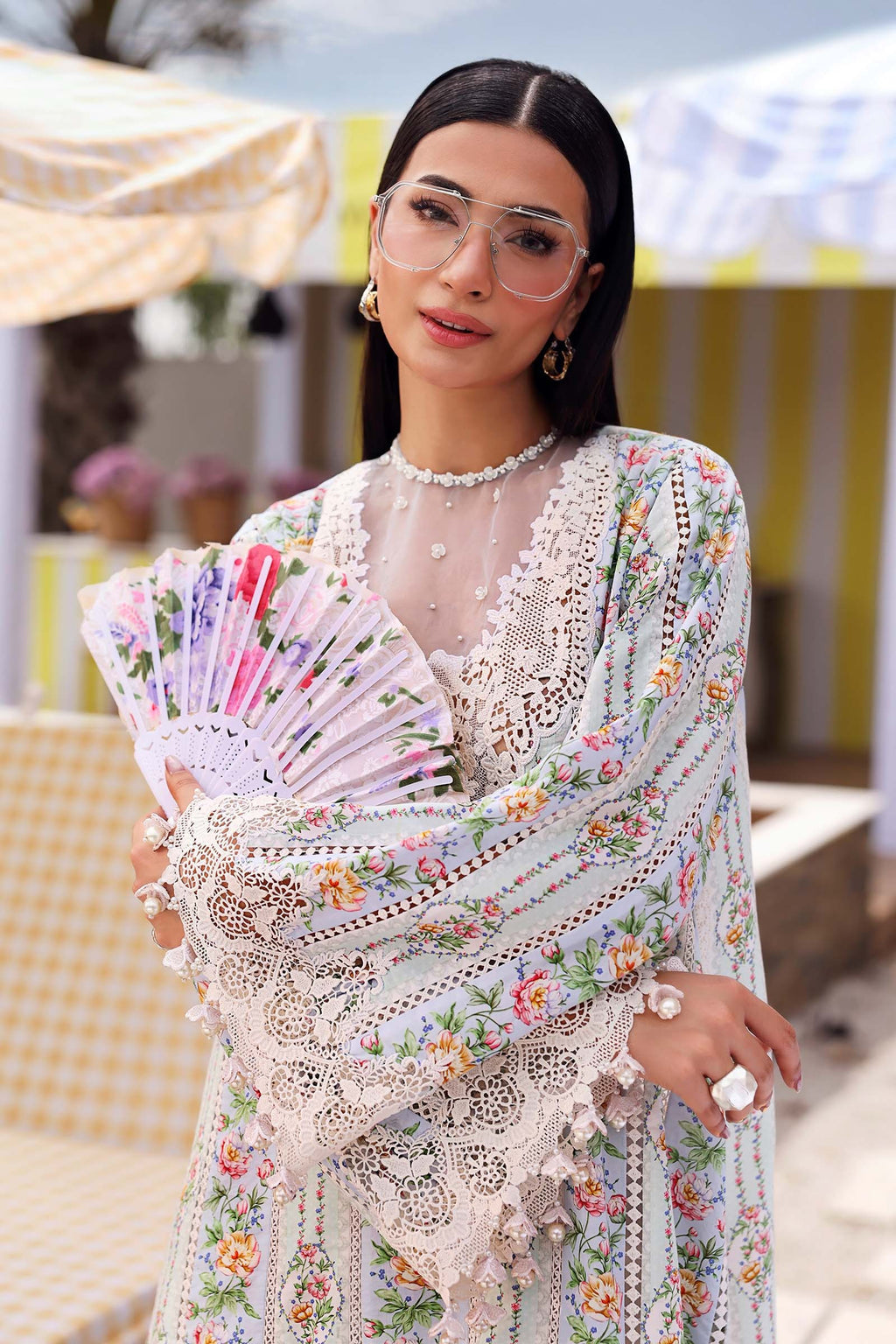 Woman in a floral dress holding a fan, standing outdoors with blurred background