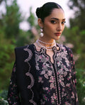 Woman wearing a black embroidered outfit with a pearl necklace against a blurred green background
