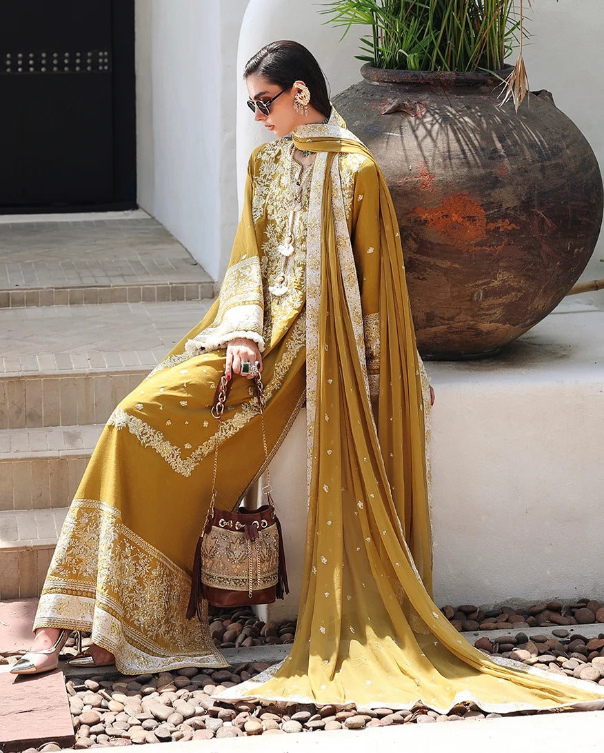 A woman wearing a traditional embroidered outfit in mustard yellow and beige sits on stone steps beside a large brown planter pot.
