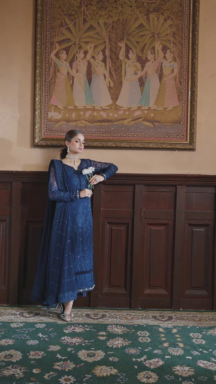 Woman in a blue dress standing in a room with a decorative wall painting.
