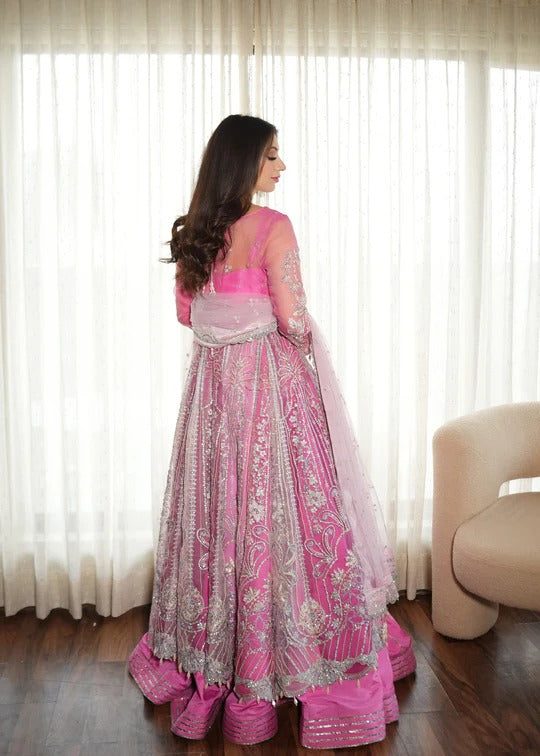 Woman in a pink and white traditional outfit standing in front of sheer curtains.