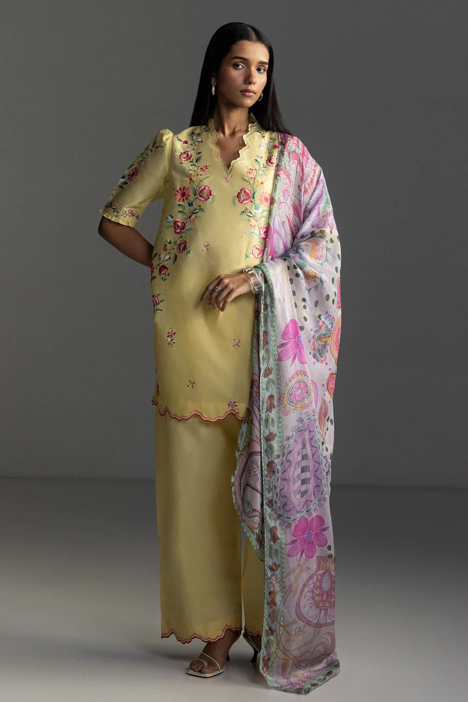 Woman wearing a traditional outfit with a yellow kurta and pink dupatta on a gray background