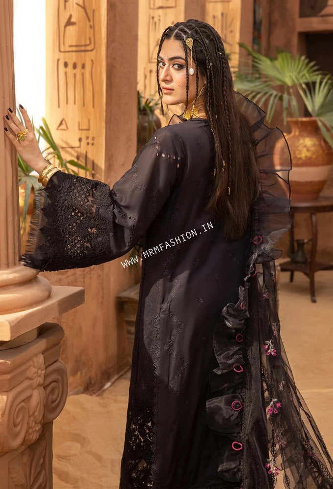 A woman modeling a black embroidered traditional outfit with sheer ruffled sleeves and a matching sheer overlay, posed in an Egyptian-themed interior setting.