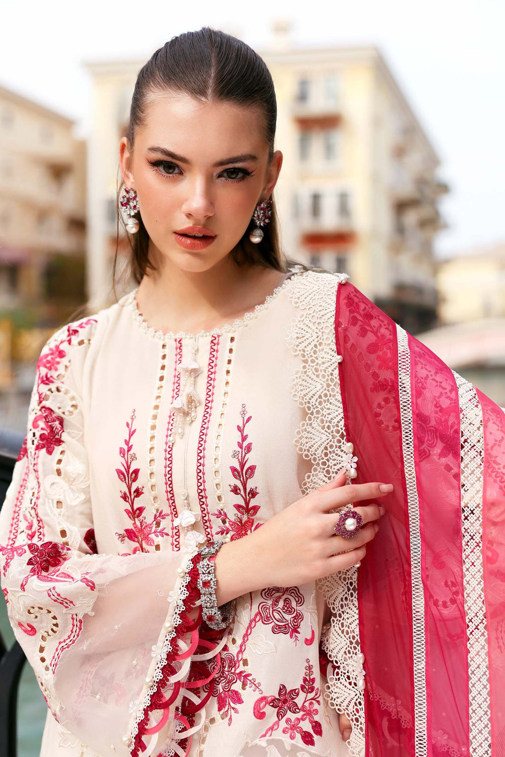 Woman wearing a white and pink embroidered traditional outfit with a blurred urban background