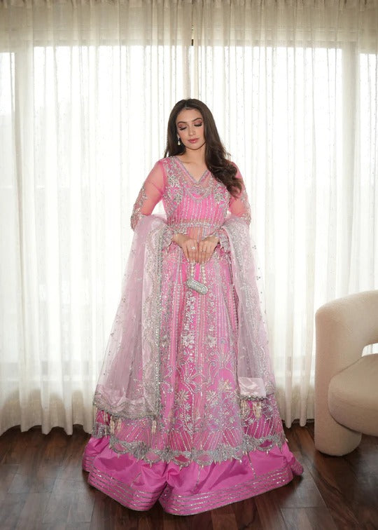 Woman in a pink traditional outfit standing in a room with white curtains.