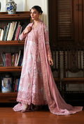 A woman models a traditional pink embroidered outfit with a matching dupatta in an indoor setting with wooden bookshelves and furniture.