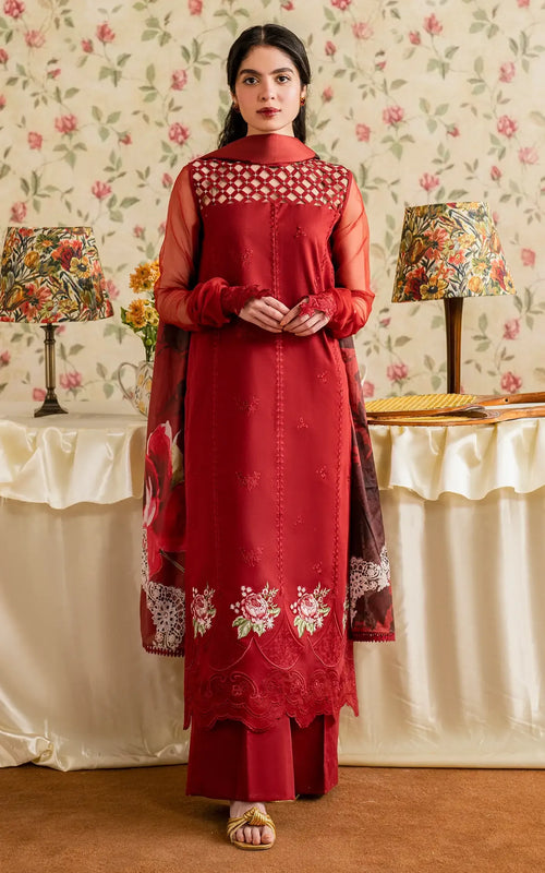 Woman wearing a red embroidered dress in a decorated room with floral wallpaper and lamps.