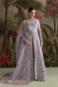 A woman models a lavender anarkali suit with intricate silver and gold floral embroidery, a matching sheer dupatta, and a high-neck embellished collar, set against a tropical jungle backdrop.