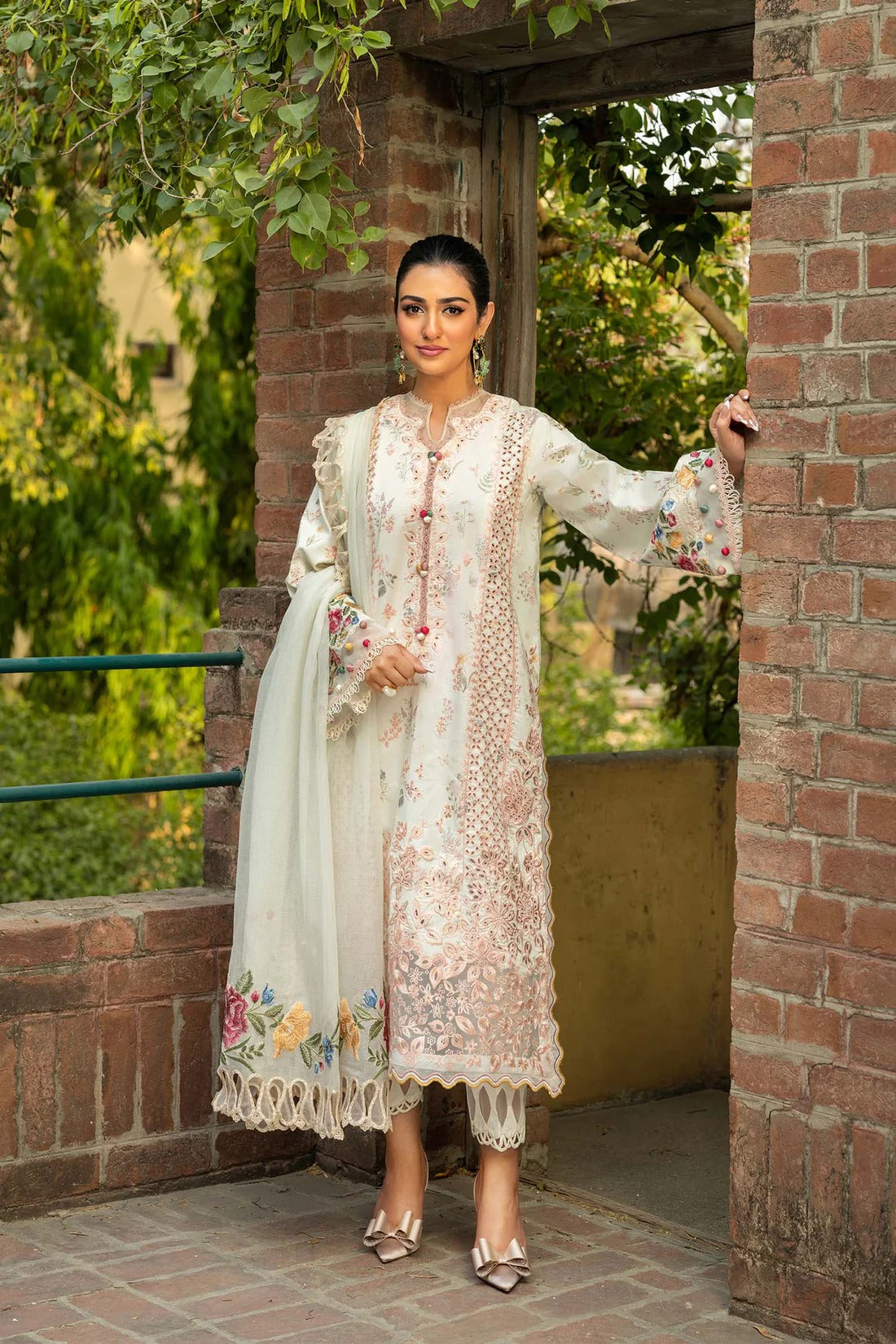 Woman in a traditional embroidered outfit standing outdoors near a brick wall.
