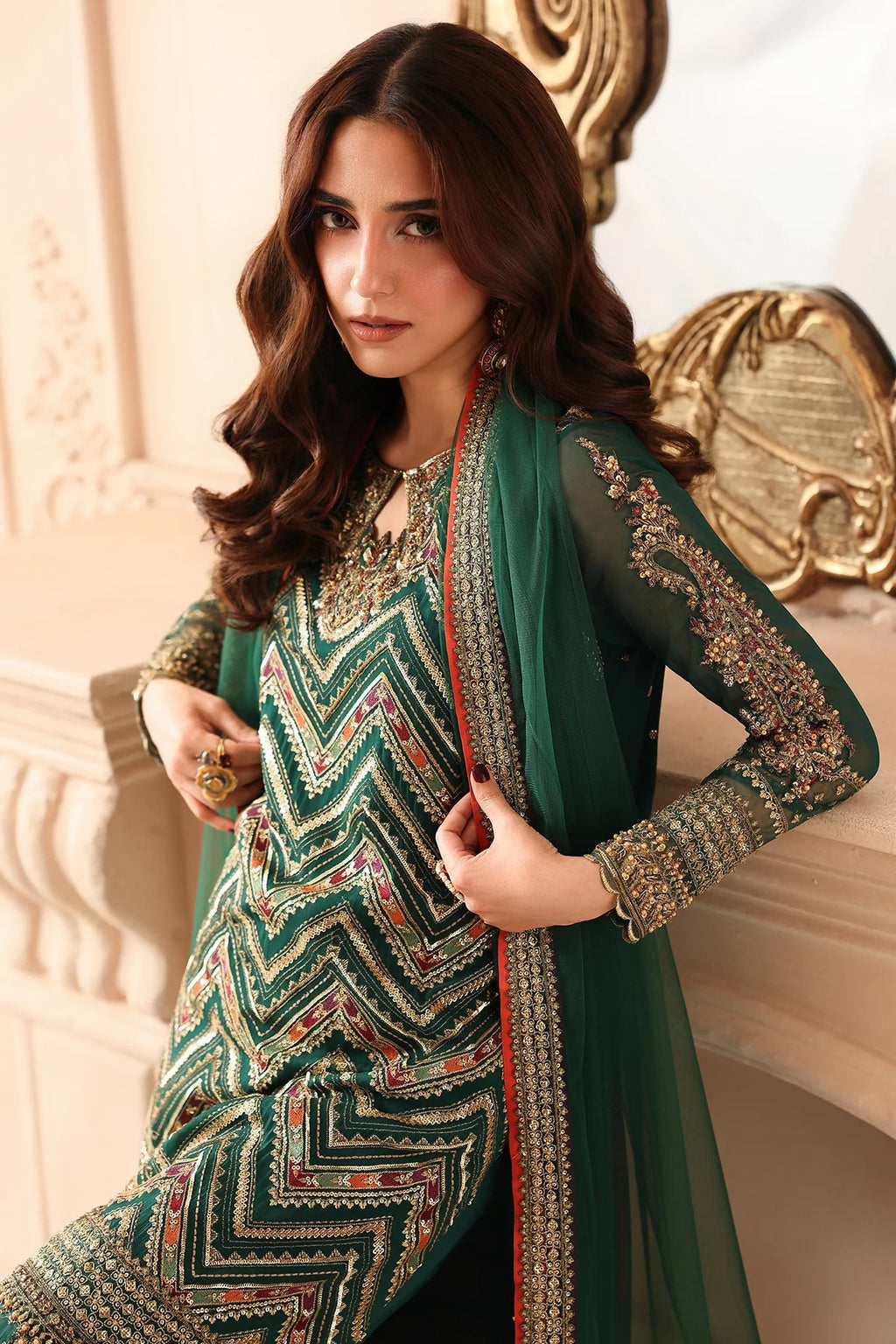 A woman models a traditional South Asian outfit featuring a green and black chevron-patterned kurta with gold embroidery, paired with a matching sheer green dupatta draped over her shoulders.