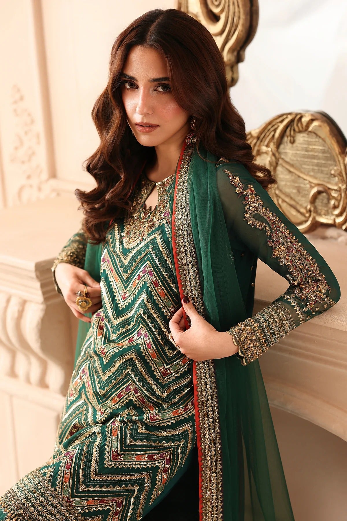 A woman models a traditional South Asian outfit featuring a green and black chevron-patterned kurta with gold embroidery, paired with a matching sheer green dupatta draped over her shoulders.