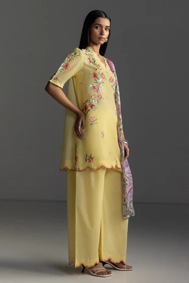 Woman wearing a yellow outfit with floral embroidery on a gray background