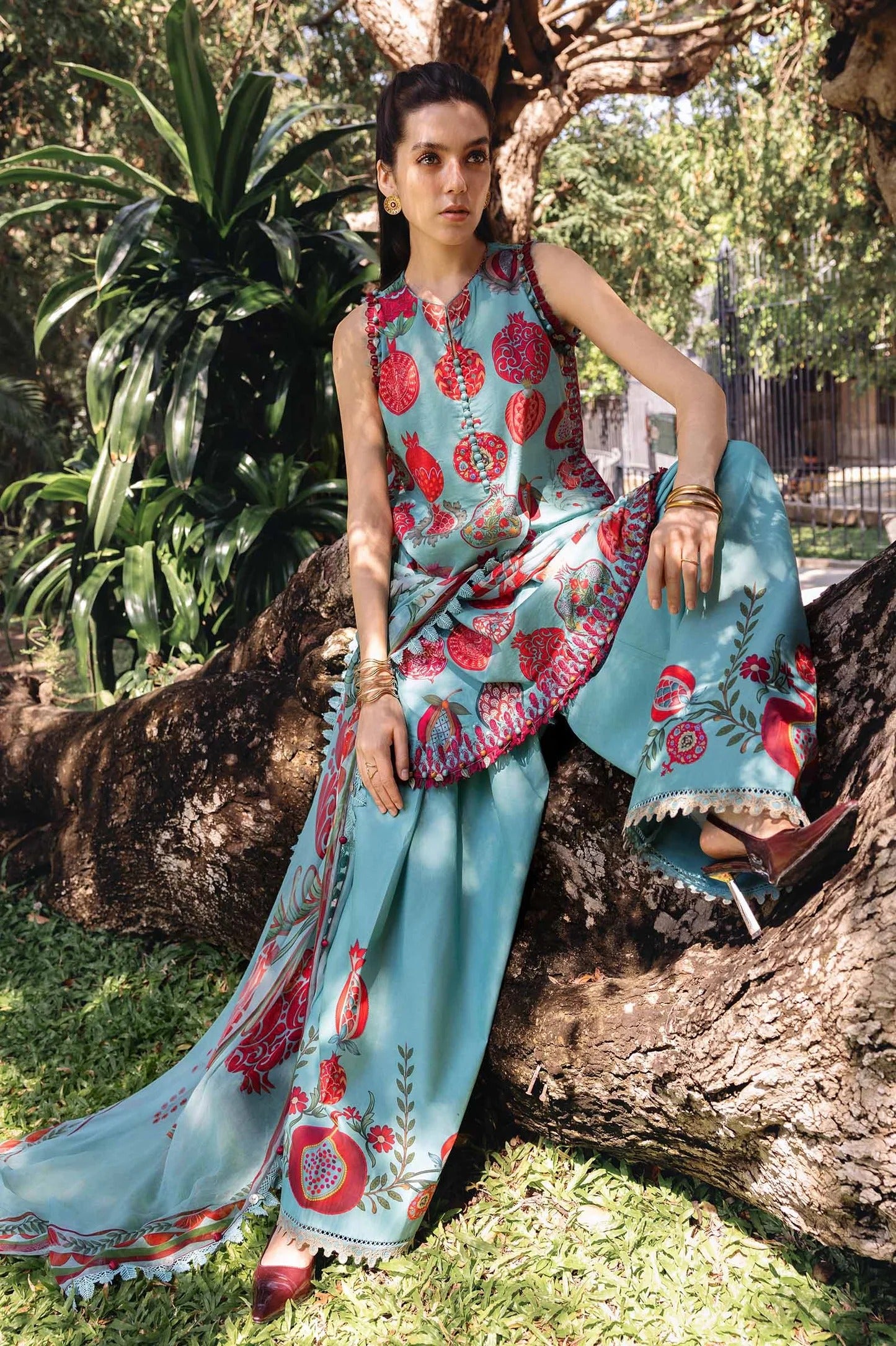 Woman in a traditional outfit with floral patterns sitting on a tree branch outdoors.