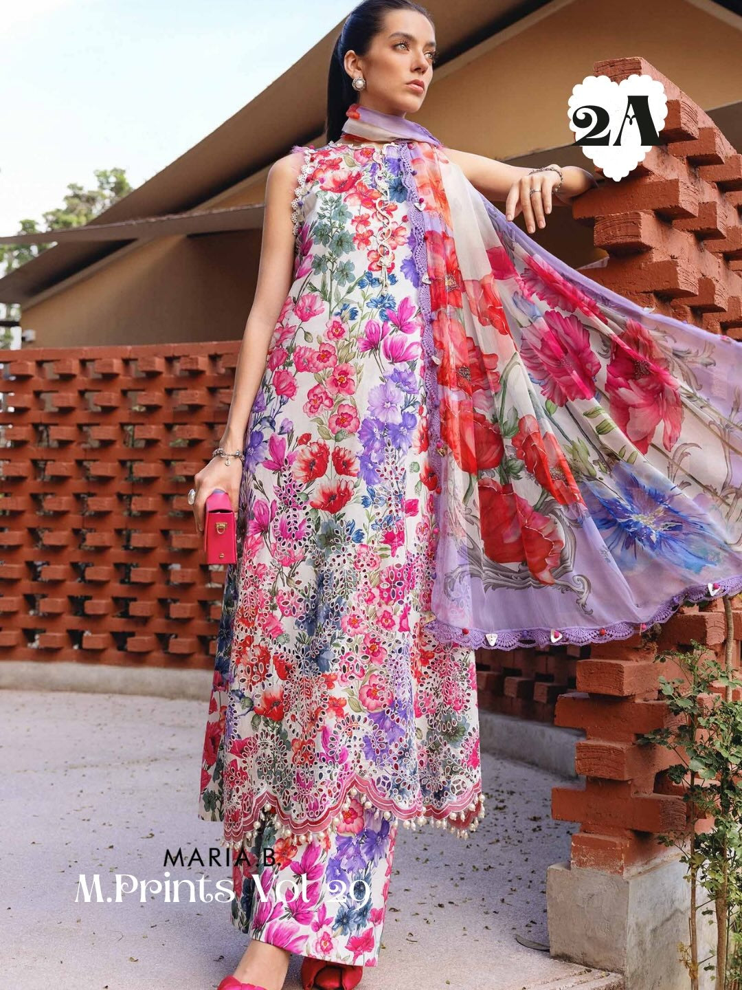 A woman models a three-piece floral print salwar kameez suit with a matching dupatta. The outfit features a white base with vibrant pink, red, purple, and green floral patterns.