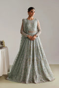 A woman modeling a heavily embroidered light sage green anarkali gown with intricate gold and silver beadwork, set against a neutral studio background.