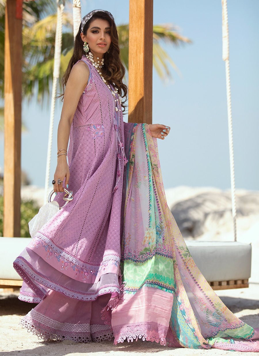 Woman in a pink traditional outfit with a colorful dupatta, standing outdoors with palm trees in the background.