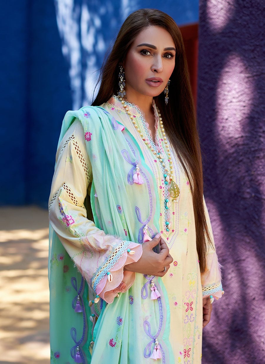 A woman modeling a traditional embroidered outfit with a mint green dupatta, cream kurta, and pink accents, set against a textured blue and purple background.