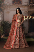 A woman models an ornate red and gold embroidered traditional Indian outfit with a matching dupatta in an indoor courtyard setting.