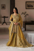 A woman models a traditional Indian ensemble consisting of a heavily embroidered mustard yellow kurta, matching flared skirt, and dupatta, set against a softly lit, vintage-style indoor room background.