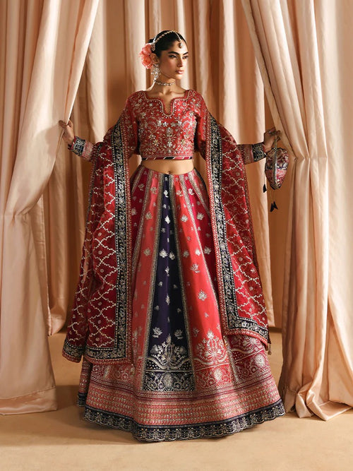 Woman in a traditional red and blue embroidered outfit standing behind beige curtains.