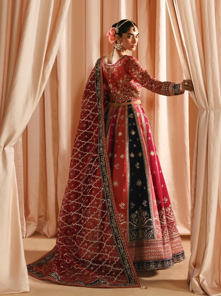 Woman in a traditional red and black embroidered outfit standing in front of pink curtains.