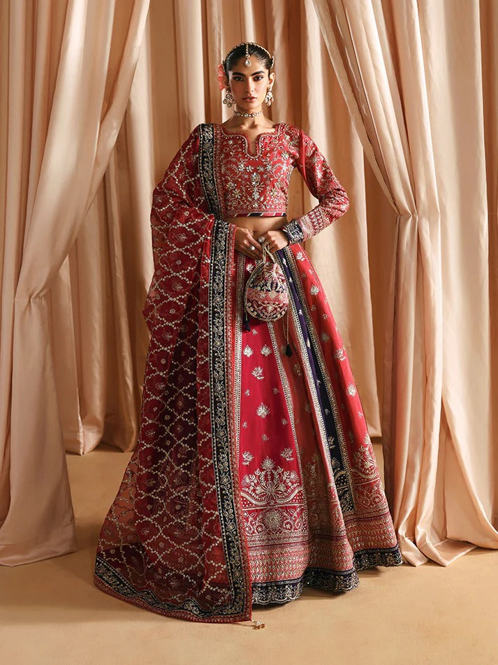 Woman in a red and black embroidered traditional outfit standing against beige curtains.