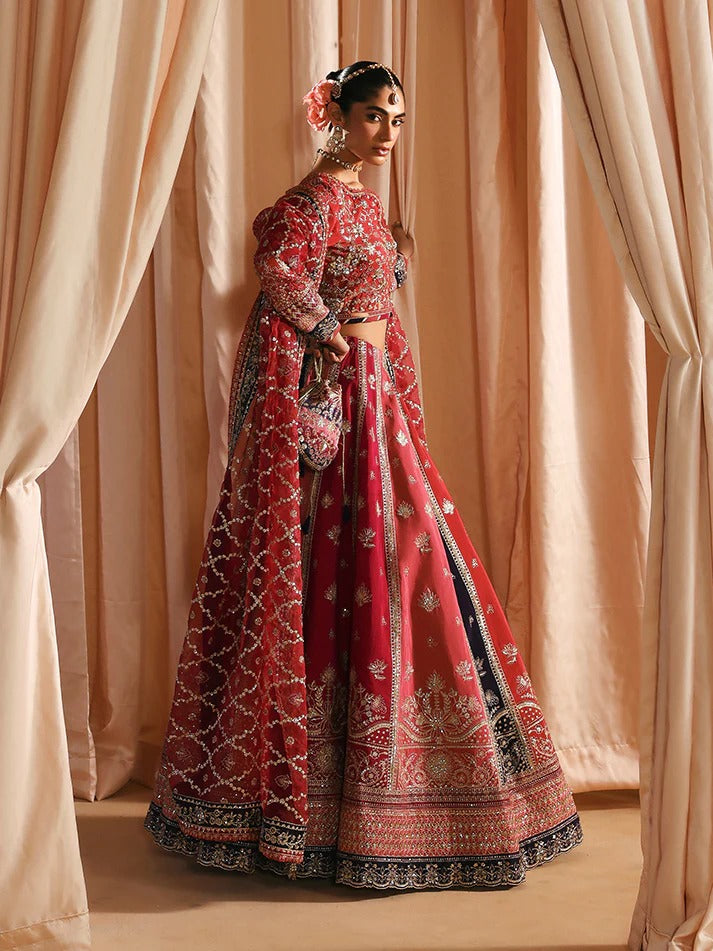Woman in a red and black embroidered traditional outfit standing against beige curtains.